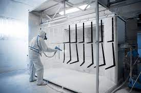 Worker in protective suit powder coating metal parts