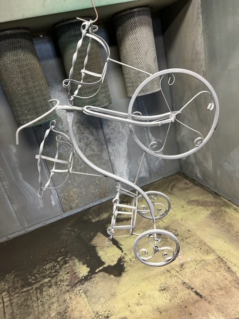 Decorative tricycle planter blasted and hung in the powder coating booth